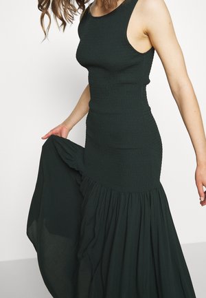 Mørkegrøn kjole med en figursyet overdel og et udvidet, tekstureret skørt. Stoffet virker blødt med et smockmønstret design i taljen.