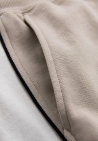 Gros plan de couches de tissu beige et blanc cassé avec des coutures visibles et une texture douce et lisse.