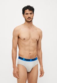 Sivé bavlnené slipy s modrým elastickým pásom s logom "PUMA"; priliehavý strih a hladká textura. Model pózuje v stoji.