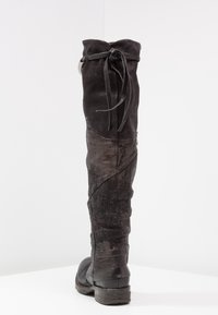 Tall black leather boots with a textured design, featuring a fabric panel and a knotted lace accent at the top and a sturdy sole.