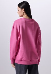 Felpa rosa con scollatura a girocollo e polsini a coste, caratterizzata da una vestibilità comoda e una texture morbida, vista da dietro.