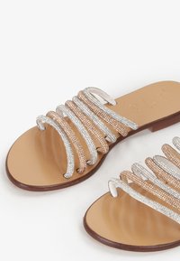 Sandali piatti con molteplici cinghie incrociate in glitter argento e oro rosa, con una suola in pelle marrone liscia e un design semplice.