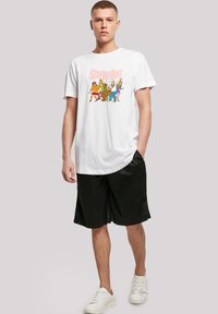 Hvit bomulls t-skjorte med et fargerikt "Scooby-Doo" grafikk. Kombinert med svarte shorts og hvite joggesko, som fremhever en avslappet stil.