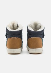 Bottes montantes bleu et marron avec doublure douce blanche, en suède texturé et toile, et une semelle en caoutchouc à motif. Fermetures Velcro sur les côtés.