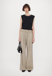 Svart ärmlös topp, beige högmidjade vida byxor med bälte och liten svart handväska. Slät tyg, neutrala färger, avslappnad passform.