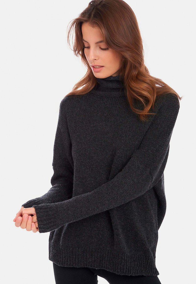 Dunkelgrauer Rollkragenpullover mit lockerer Passform, strukturiertem Stoff, gerippten Bündchen und seitlichen Schlitzen. Kombiniert mit schwarzen Leggings.