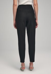 Zwarte high-waisted broek met een tailored fit, voorzien van een enkele achterzak en subtiele plooien, gecombineerd met gespsandalen met hak.