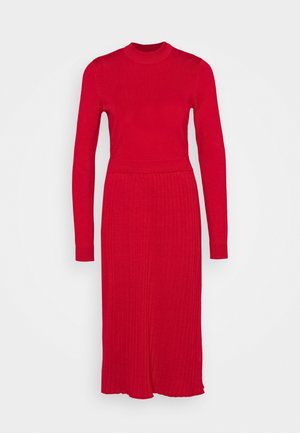 Robe tricotée rouge à manches longues, texture côtelée, col haut et corsage ajusté se transformant en une base évasée.