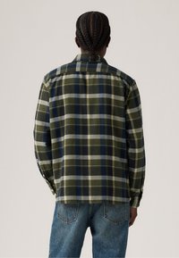 Groene en marineblauwe geruite flanellen shirt met knoopdetails, lange mouwen en een rechte snit. De achterkant toont een zachte textuur en een contrasterend patroon.
