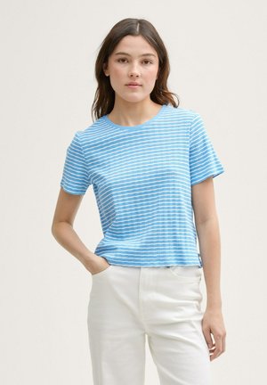 Maglietta in cotone azzurro chiaro con righe bianche orizzontali, maniche corte, scollatura rotonda e una vestibilità rilassata. Indossata con pantaloni bianchi.