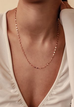 Halskette aus Roségold mit kleinen, verbundenen geometrischen Formen. Getragen an einem neutralen Ausschnitt mit feinem Rippendetail.