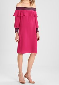 Vestido fucsia con escote off-the-shoulder, cuello con volantes, mangas largas con acentos a rayas, y corte recto que llega hasta la mitad de la pantorrilla.