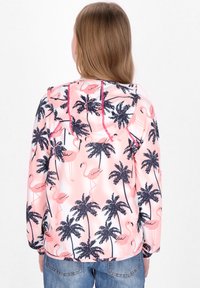 Giacca leggera rosa con cappuccio, caratterizzata da una stampa tropicale di palme blu scuro e fenicotteri rosa, realizzata in un tessuto liscio e lucido.