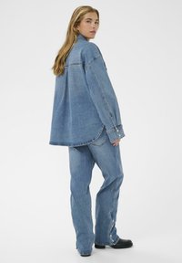 Veste en denim oversized et jeans assortis en bleu moyen. Comprend un col pointu, des fermetures à boutons et des ourlets légèrement effilochés. Texture douce.