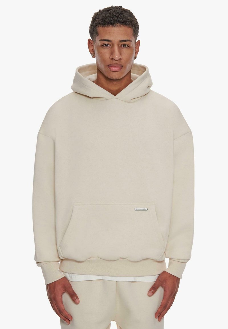 Beige Kapuzenpullover mit strukturierter Oberfläche, im Oversized-Fit und mit Fronttasche. Besitzt einen gewellten Saum und ein aufgenähtes Etikett.