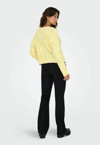 Pull jaune tricoté coupé avec un motif de tricot en relief et un ourlet côtelé, associé à un jean noir évasé et des bottes noires robustes.
