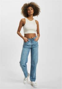 Ingekorte crèmekleurige tanktop gecombineerd met lichtblauwe hoge taille jeans. Het model draagt witte sneakers. Textiel met structuur en een relaxte pasvorm.