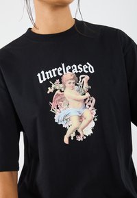 Svart bomull T-skjorte med et grafisk motiv av en kjærkomme omgitt av blomster og ordet "Unreleased" i fet hvit tekst over.