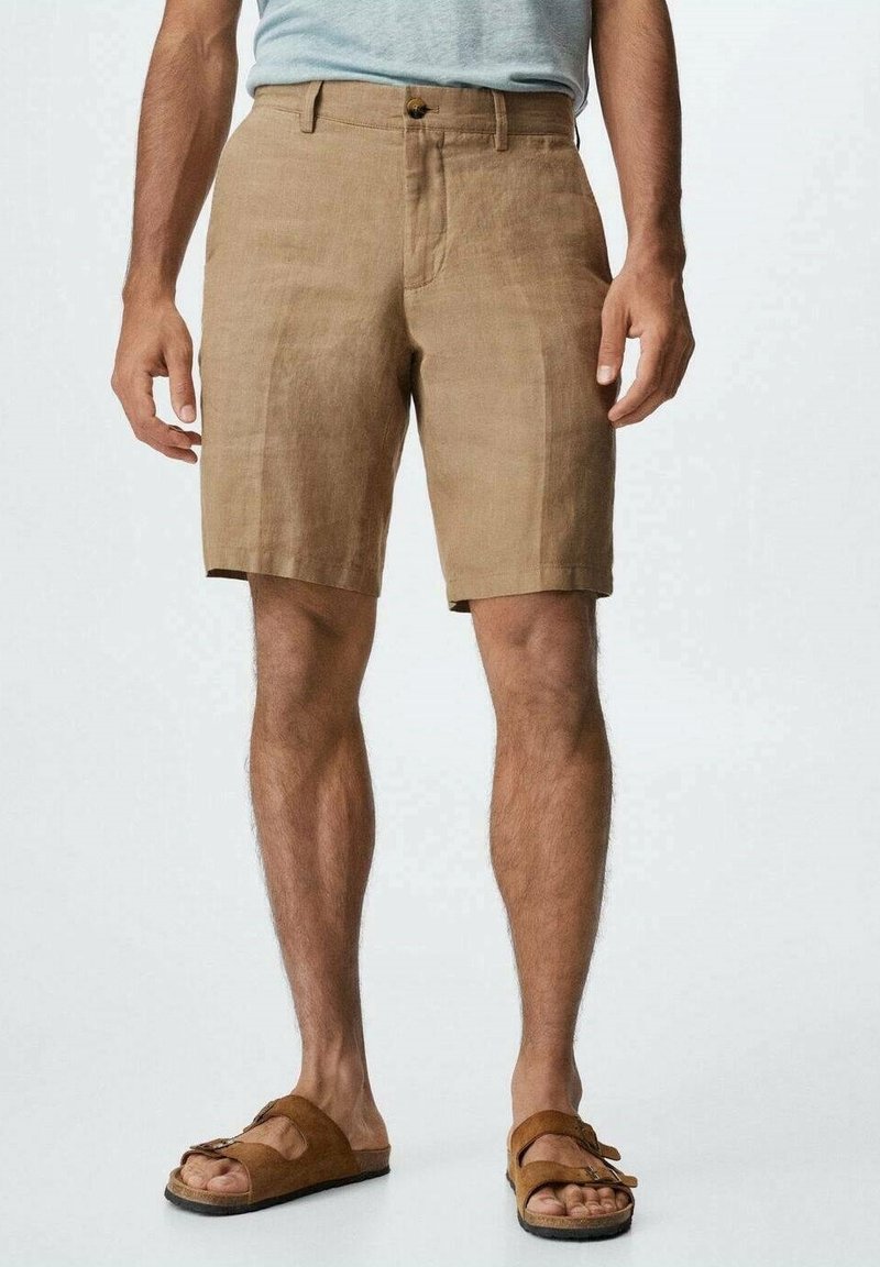 Shorts en lin brun à coupe décontractée, dotés d'une fermeture à bouton, de poches latérales et d'une texture lisse. Portés avec des sandales brunes.