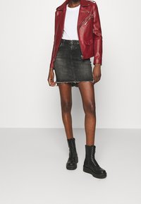 Červená kožená motocyklová bunda, bílý tričko, černá denimová minisukně s roztrhaným lemem a černé platformové boty na šněrování.