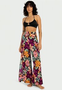 Un top scurt negru cu o decupare frontală, asortat cu pantaloni largi florali în culori vibrante, având flori mari multicolore pe un fundal întunecat.