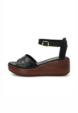 Sandalia cuña negra de piel con puntera abierta, suela plataforma con textura de madera y correa ajustable en el tobillo con hebilla dorada.