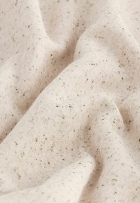 Tela de color beige claro con una textura suave, que presenta motas dispersas de verde oscuro y marrón claro en toda la superficie.