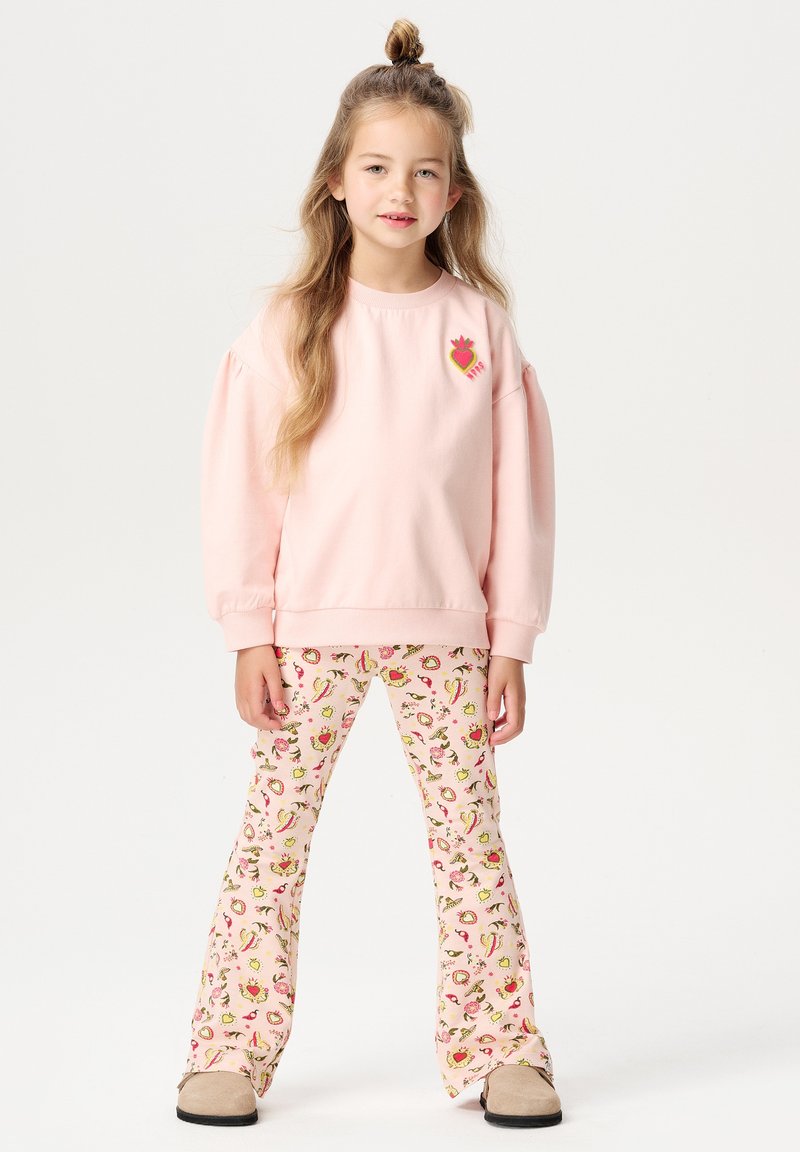 Helles rosa Sweatshirt mit Puffärmeln und einem Erdbeer-Motiv auf der Brust, kombiniert mit weit geschnittenen Hosen, die ein buntes Fruchtmuster aufweisen.