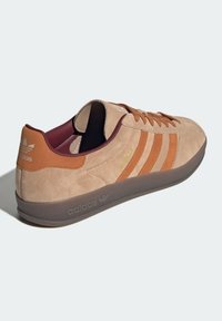 Beigefärgade mockasneakers med bruna detaljer, utrustade med tre sidostripes, texturerad sula och lågprofil design. Logotyp på hälen och tungan.