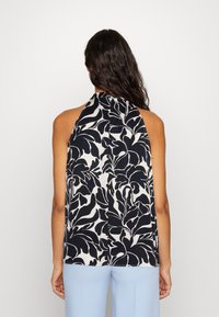 Vista posteriore di una blusa senza maniche caratterizzata da un motivo floreale nero su sfondo beige, con un collo alto e una vestibilità rilassata.