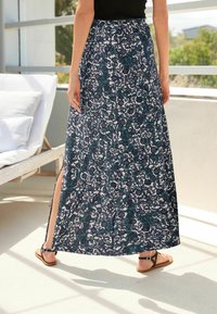 Jupe longue et fluide en bleu marine avec des motifs floraux et paisley blancs complexes. Présente une fente sur le côté et une taille élastique confortable.