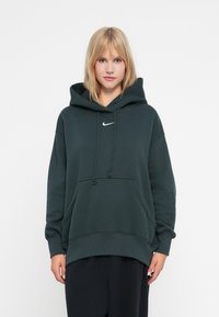 Žalias džemperis su priekinėmis kišenėmis ir raišteliais. Priekyje yra mažas baltas Nike logotipas. Pagamintas iš minkštos, tekstūrinės medžiagos.