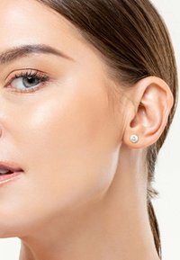 Silberner Steckerohrring mit einem glatten, runden Design. Nahaufnahme von Haut mit natürlicher Oberfläche, die den Ohrring hervorhebt. Schlichte, moderne Ästhetik.