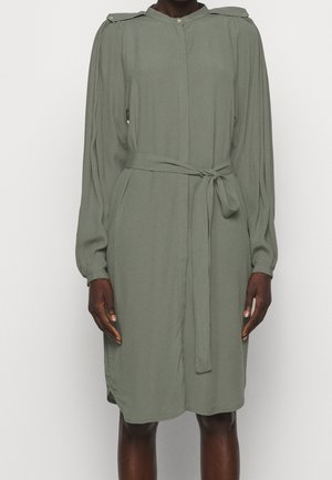 Długa sukienka z długim rękawem w oliwkowym kolorze, z paskiem, pagonami na ramionach i marszczonymi mankietami, noszona przez osobę stojącą na jednolitym tle.