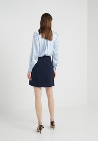 Light blue satin blouse with long sleeves, paired with a navy knit skirt. The outfit features a sleek, tailored silhouette and minimal detailing.