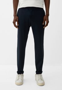 Marineblauwe trousers in zachte stof met een slim fit, voorzien van riemlussen en een ritssluiting, gecombineerd met lichtgekleurde sneakers.