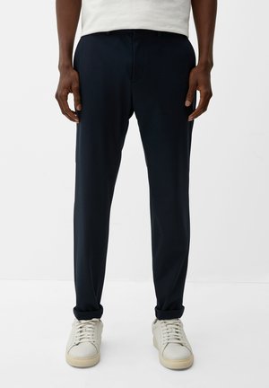 Navyblaue Hose aus weichem Stoff mit slim fit, ausgestattet mit Gürtelschlaufen und einem Reißverschluss, kombiniert mit hellen Sneakers.