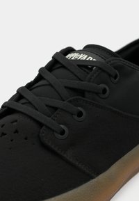 Baskets décontractées noires avec dessus en tissu, lacets noirs passés dans des œillets métalliques, et semelle en caoutchouc marron clair.