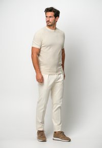 Beige Kurzarmpullover aus weichem Material, kombiniert mit cremefarbenen Hosen. Die Schuhe haben eine braune Wildleder-Oberfläche und eine weiße Sohle.