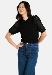 Zwarte korte mouwen top met textuur en bloemenkant mouwen, gecombineerd met hooggetailleerde blauwe denim jeans. Eenvoudige ronde halslijn; casual pasvorm.