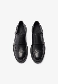 Black leather shoes with brogue detailing, featuring a strap and buckle across the upper. Rounded toe and textured side accents.