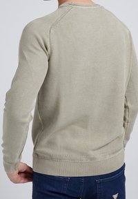 Pull en maille beige avec un motif texturé, poignets et ourlet côtelés, et un col rond classique, vu de dos.