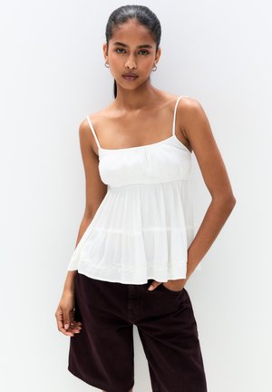 White, lightweight sleeveless top with a gathered bodice and delicate embroidery at the hem, paired with dark burgundy shorts.