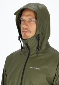Olivgrüne wasserdichte Jacke mit Kapuze, verstellbaren Kordeln und einem schwarzen Reißverschluss. Mit 'SWEDEMOUNT'-Logo auf der linken Brust.