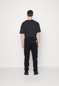 Černé tričko s krátkým rukávem a černé kalhoty z pohledu zezadu. Neformální střih s rovnými nohavicemi, nošeno s černými teniskami.