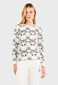 Sudadera blanca con un patrón de búhos de dibujos animados coloridos, cuello redondo y mangas largas. Tejido suave. Combinada con pantalones de lounge de colores claros.