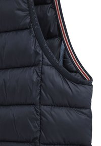 Granatowa kamizelka puchowa z pikowanym wzorem, z okrągłym kołnierzem i czerwonymi, białymi oraz niebieskimi paskami wzdłuż dekoltu.