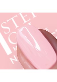 Lys rosa neglelakk påført en negl med en jevn og glansfull finish; bakgrunnen har myk rosa branding.