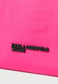 Różowa nylonowa torba z wyraźnym czarnym logo "KARL LAGERFELD JEANS", o gładkim, błyszczącym wykończeniu i minimalistycznym designie.