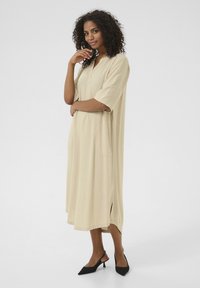 Robe midi couleur crème avec des manches courtes retroussées, un col rond, des poches latérales et un ourlet droit avec de légentes fentes sur les côtés.
